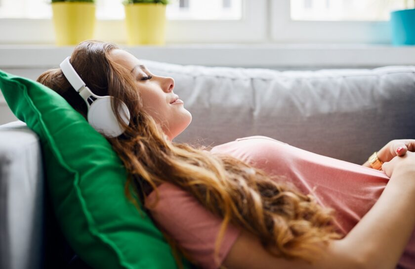 Portrait of a beautiful young woman lying on sofa with headphones on and closed eyes, relaxing
